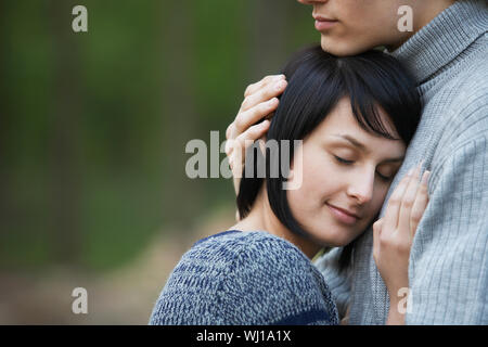 Closeup side view of a young woman laying head on man's chest against blurred background Stock Photo
