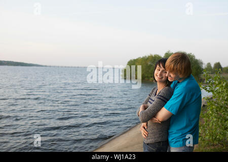 Side view of a smiling young couple embracing on lakeshore Stock Photo