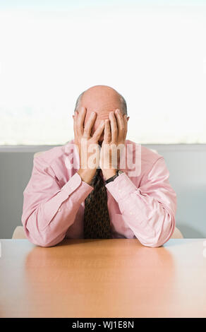 Stressed businessman with head in hands sitting at office desk Stock Photo