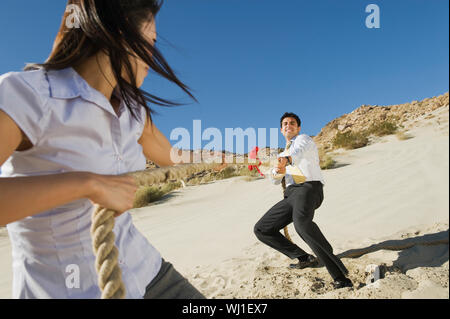 Businessman and businesswoman playing tug of war in desert Stock Photo
