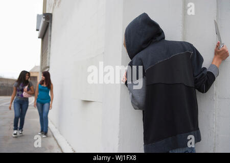 Robber with knife hiding behind corner and waiting for two girls Stock Photo