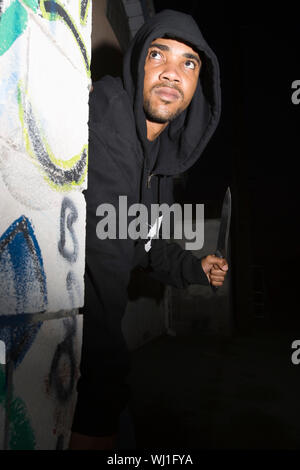 Robber with knife hiding behind corner Stock Photo