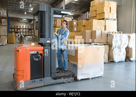 Worker operating forklift stacking cardboard boxes on distribution ...