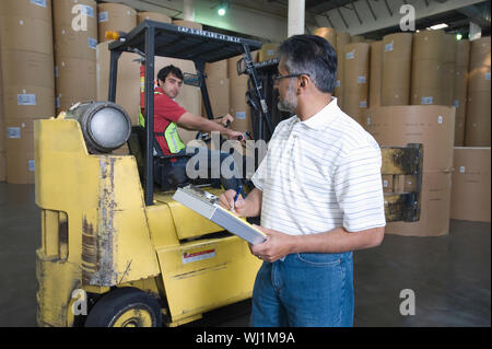 Supervisor looking at man in forklift truck at newspaper factory Stock Photo