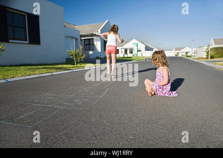 Two young girls playing hopscotch on the street along houses Stock Photo
