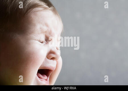 Closeup of a baby girl crying against gray background Stock Photo