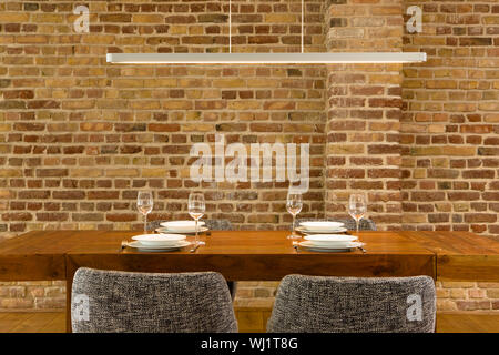 View of wineglasses and plates on dining table against brick wall in modern house Stock Photo
