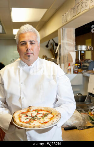 Portrait of a confident mid adult chef holding pizza in commercial kitchen Stock Photo