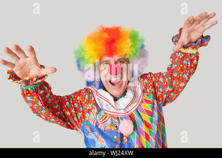 Portrait of funny clown with arms raised and mouth open against colored background Stock Photo