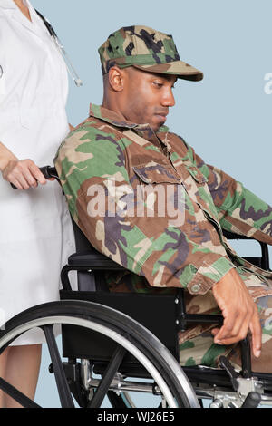 Sad US Marine Corps soldier wearing camouflage uniform in wheelchair assisted by female nurse Stock Photo