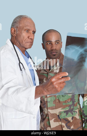Senior doctor with US Marine Corps soldier looking at x-ray report over light blue background Stock Photo