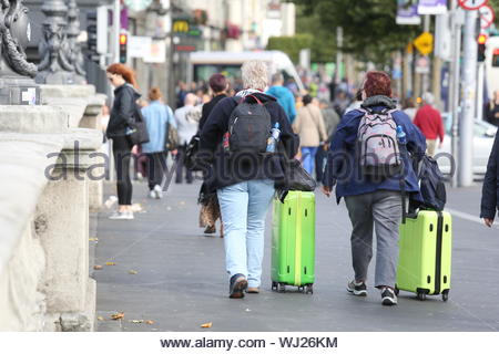 Two people push large green wheelie cases across O'Connell bridge in Dublin's inner city on a summer's day Stock Photo