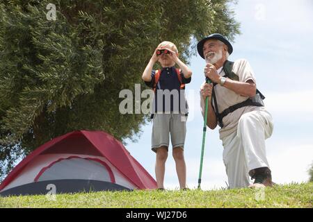 Grandfather and grandson with backpack bird watching in front of tent Stock Photo
