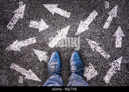 Sneaker shoes and arrows pointing in different directions on asphalt ground, choice concept Stock Photo