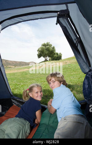 Portrait of happy brother and sister lying in tent on vacations Stock Photo