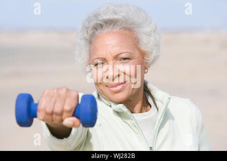 Portrait an African American senior woman exercising with dumbbells at beach Stock Photo