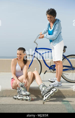 Full length of a senior woman with bicycle looking at daughter wearing skate shoe against sky Stock Photo