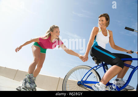 Low angle view of a young woman on bike pulling friend on in-line skates Stock Photo