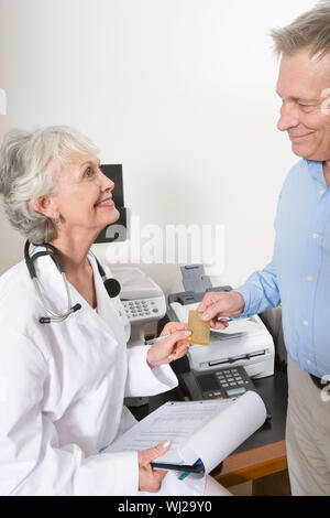 A senior female doctor accepting payment through credit card from the patient in clinic Stock Photo