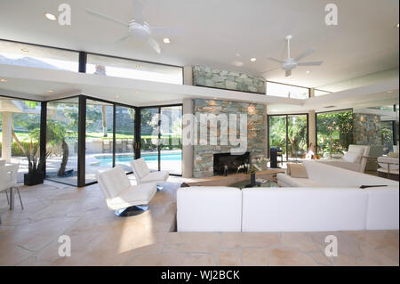 Sunken seating area and exposed stone fireplace in spacious living room with view of swimming pool at home Stock Photo