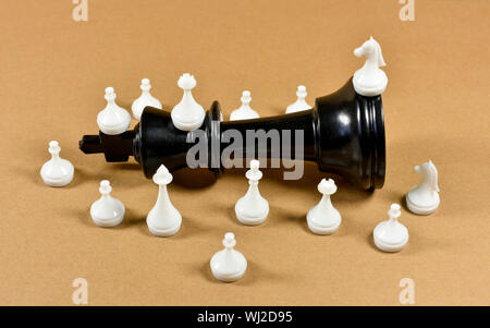 Black king chess piece fallen on a board with white small chess pieces surrounding it, conceptual image about leadership , competition and business Stock Photo