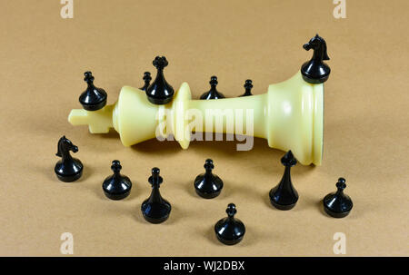 White king chess piece fallen on a board with black small chess pieces surrounding it, conceptual image about leadership , competition and business Stock Photo