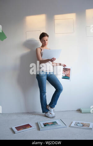 Full length of young woman decides on pictures to mount on wall Stock Photo