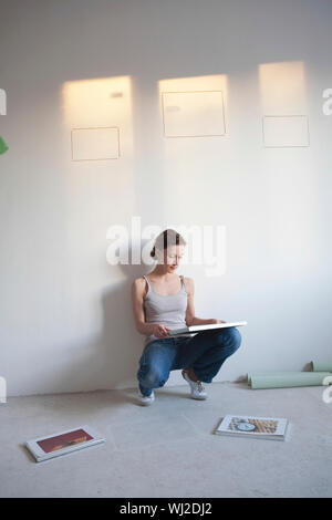 Full length of young woman decides on pictures to mount in new apartment Stock Photo