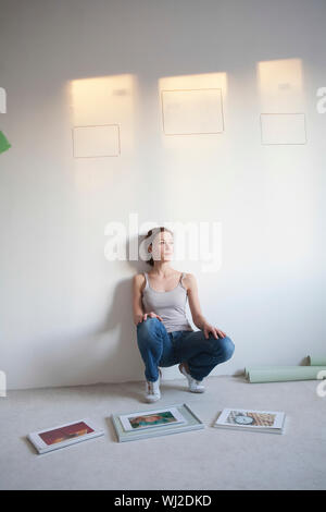 Full length of thoughtful young woman decides on pictures to mount in new apartment Stock Photo