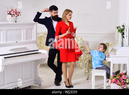 Kid growthing in welfare. Mother and father stands near piano, watching while their son on busy face drawing, luxury interior. Proud parents concept. Stock Photo
