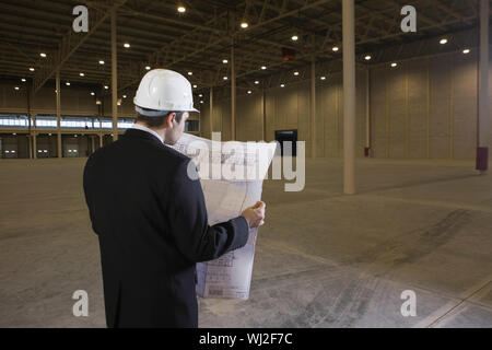 Rear view of male architect looking at blueprint in empty warehouse Stock Photo