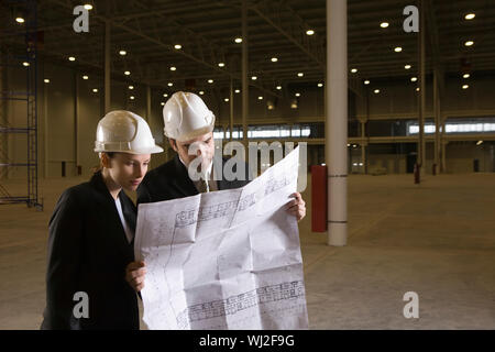 Two young architects looking at blueprint in empty warehouse Stock Photo