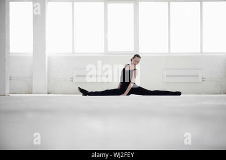 Full length of female dancer doing splits in empty warehouse Stock Photo