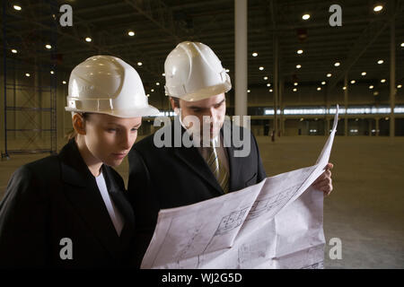 Two young architects looking at blueprint in empty warehouse Stock Photo