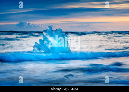 Iceberg pieces washed by waves on Diamond beach in Iceland during sunset Stock Photo