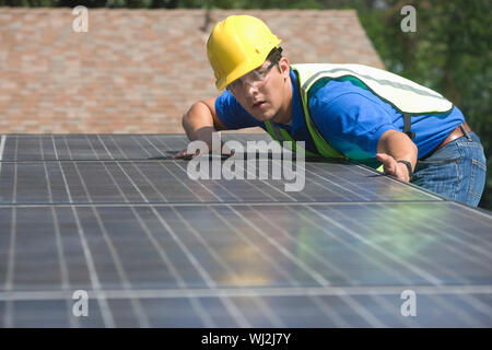 Young maintenance worker installing solar panels on rooftop Stock Photo