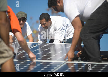 Group of multiethnic engineers placing solar panel on rooftop Stock Photo