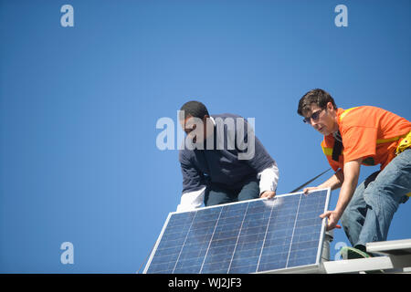 Low angle view of engineers fixing solar panel against blue sky Stock Photo