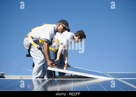 Side view of multiethnic engineers placing solar panel against blue sky Stock Photo