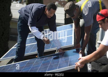 Multietchinc engineers placing solar panel together on rooftop Stock Photo