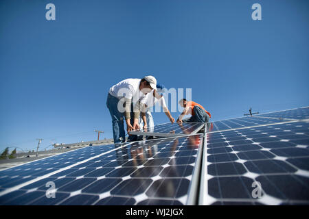 Interracial engineers placing solar panel against clear blue sky Stock Photo