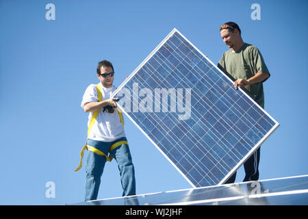 Young interracial engineers holding solar panel againat blue sky Stock Photo