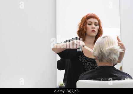Hair stylist cutting senior woman's hair in salon Stock Photo