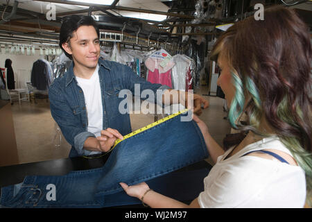Male owner showing jeans measurement to female client in laundry Stock Photo