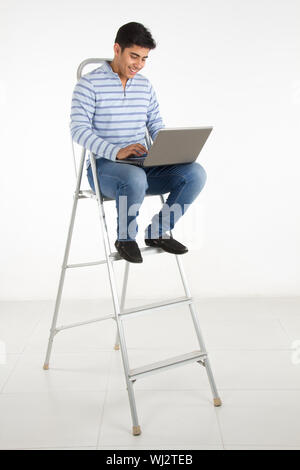 Young man sitting on a step ladder using a laptop Stock Photo