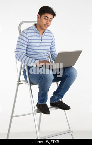 Young man sitting on a step ladder using a laptop Stock Photo