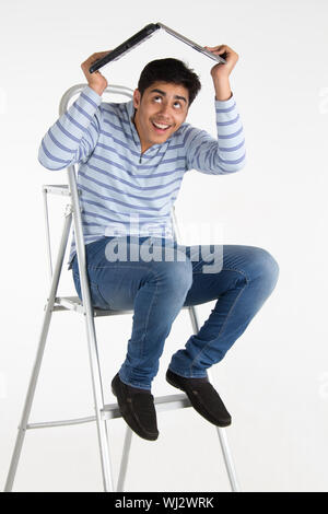 Young man holding a laptop above his head as a shelter Stock Photo