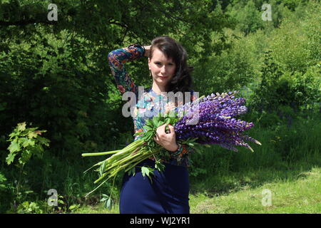 Portrait Of Woman With Hand In Hair Holding Lavenders While Standing On Field Against Trees