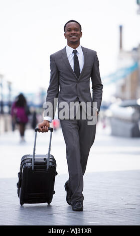 Portrait of African American businessman smiling and pulling suitcase Stock Photo