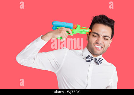 Frustrated man holding toy gun to his head over red background Stock Photo